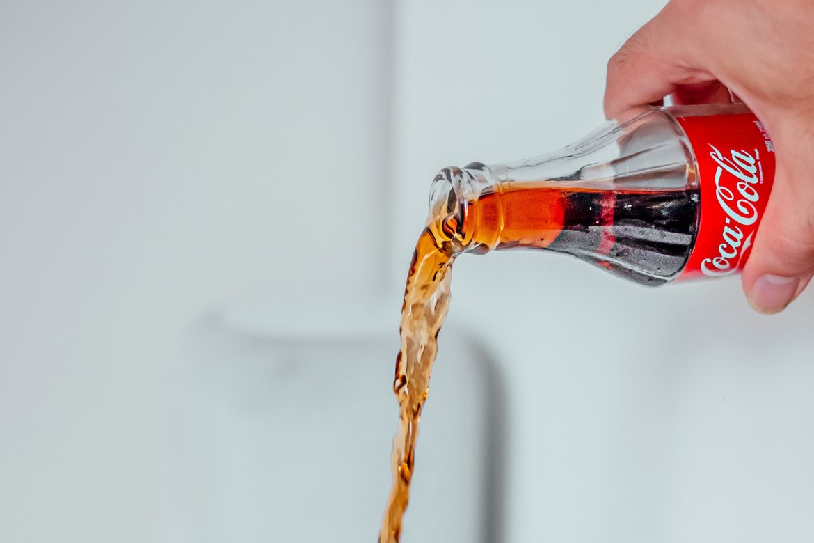 Ręka trzymająca poziomo odkręconą butelkę Coca-Coli